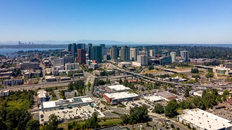 Aerial view of Bellevue, WA, with skyscrapers, highways, and Lake Washington under a clear sky.