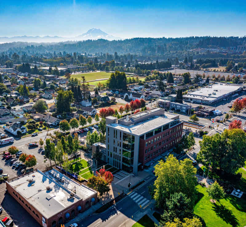 Aerial view of a town with a modern building, trees, and Mount Rainier in the distance.
