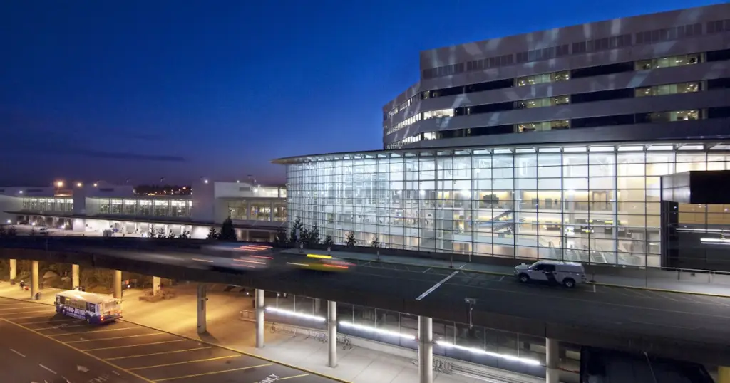 Modern Seatac, WA airport terminal at dusk with glass facade and moving vehicles.