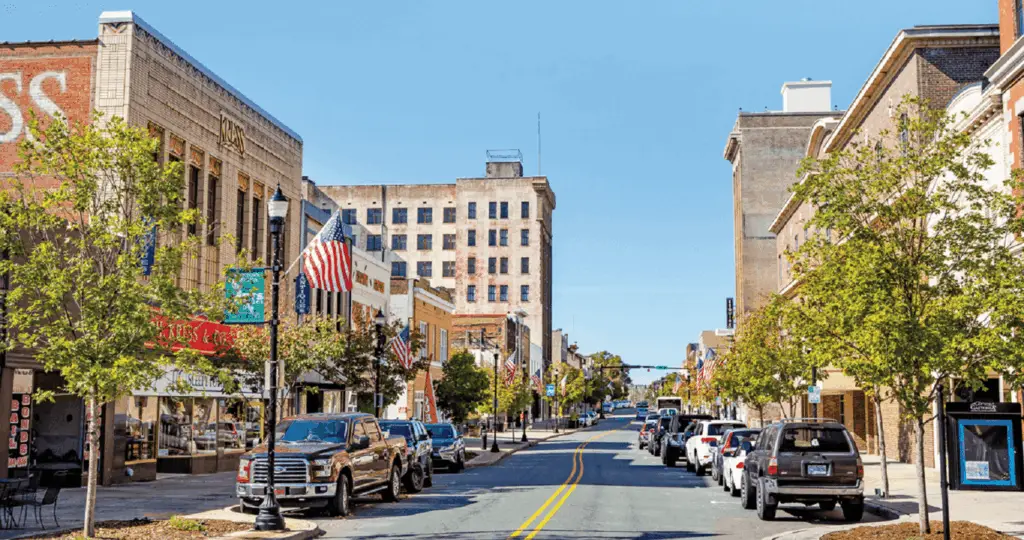 A lively street scene of downtown Gastonia, featuring trees, parked cars, and American flags, reflecting the essence of Website Design Gastonia NC.