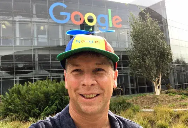 Person wearing a colorful “Noogler” propeller hat in front of the Google headquarters building