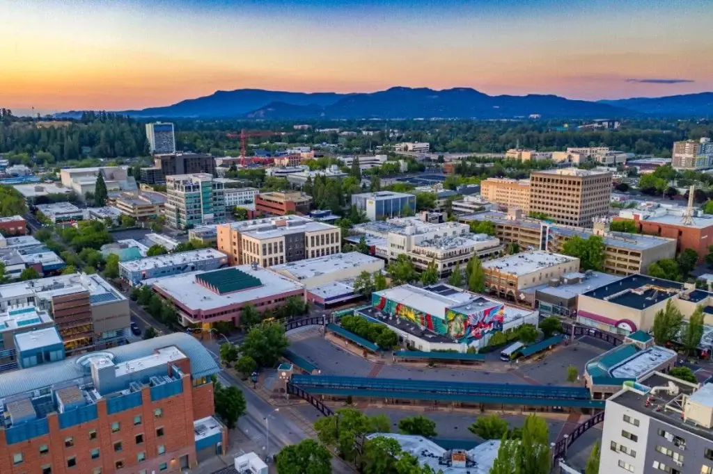 An aerial shot of the Eugene, OR, skyline with commercial buildings, a vibrant mural, and distant mountains at sunset. For superior digital solutions, consider Website Design Eugene OR.