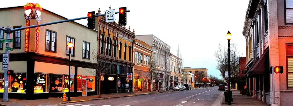 Downtown Albany, OR street at dusk with historic buildings, traffic lights, and warm glowing shop windows. Website Design Albany OR is key.