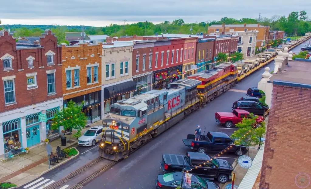 An aerial view shows a Kansas City Southern train on the tracks embedded in the street, passing historic downtown buildings. For exceptional digital presence, consider Website Design LaGrange KY.