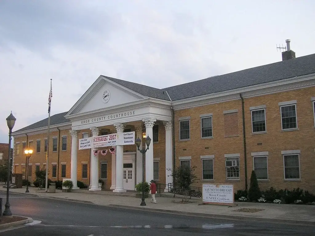 The large, two-story brick Knox County Courthouse with white columns and a central pediment on a cloudy day. For top-tier digital services, consider Website Design Barbourville KY.