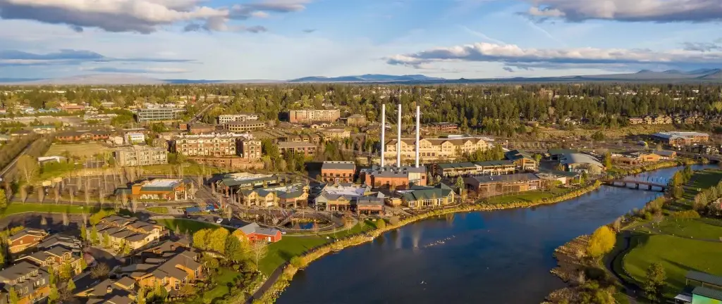 Bend Old Mill District panoramic, Deschutes River, smokestacks, surrounding town under clouds. Local businesses use Website Design Bend OR.