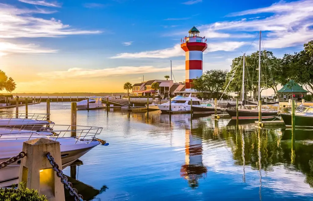 Stunning view of Hilton Head Island's lighthouse with boats and sunset reflection, ideal for Website Design Hilton Head Island SC.