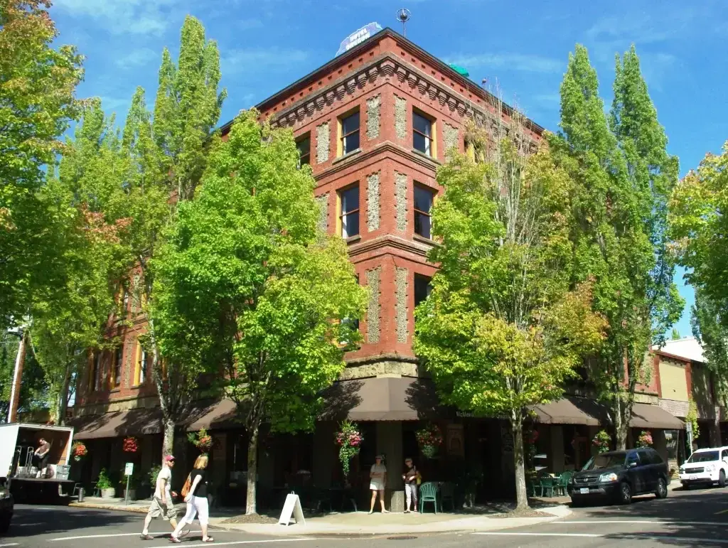 Historic brick building on a sunny downtown street corner in McMinnville OR, surrounded by tall green trees. Enhance local presence with expert Website Design McMinnville OR: Web Design & Development.