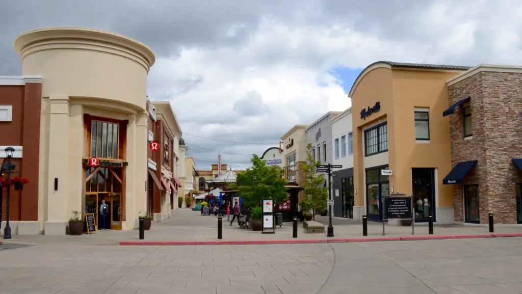 Outdoor lifestyle shopping center with curved sidewalks, two-story buildings, and retail stores under a cloudy sky near Tigard OR.